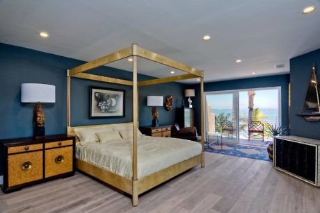 Elegant bedroom with a gold canopy bed and ocean view terrace.