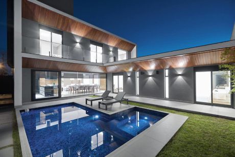 Modern house exterior at night with illuminated pool and patio area.