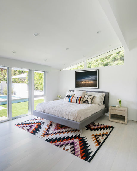 Bright bedroom with geometric rug, minimalistic furniture, and pool view.