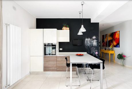 Contemporary kitchen with black wall, white cabinets, and colorful art.