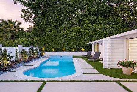 Elegant backyard with a shaped pool, loungers, and lush greenery at