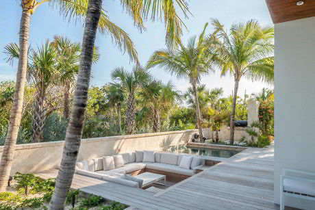 Modern outdoor patio with sectional sofa, wooden deck, and tropical plants.