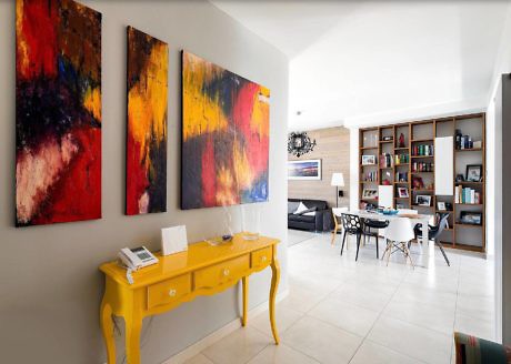 Modern living room with abstract art, yellow console table, and open bookshelf.