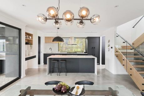 Modern kitchen interior with central island, bubble pendant lights, and adjacent staircase.