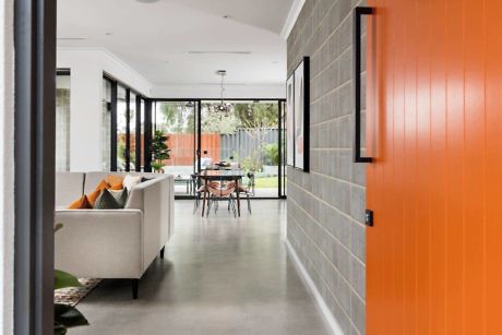 Sleek hallway with bold orange door and view into living space.