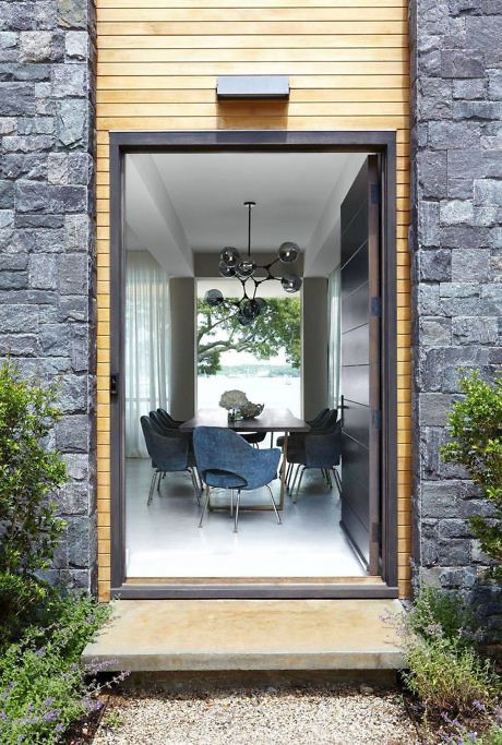 Modern dining room viewed through a tall doorway framed by stone and wood.