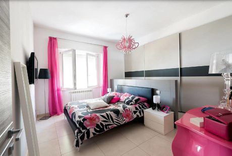 Modern bedroom with pink curtains, floral bedding, and stylish lamp.