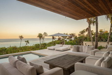 Luxurious patio with seating, pool, and ocean view at dusk.