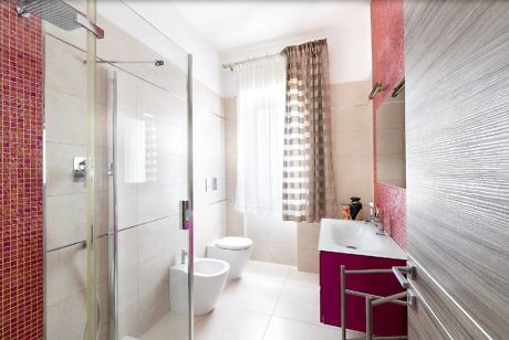 Modern bathroom with glass shower, pink tiles, and white fixtures.