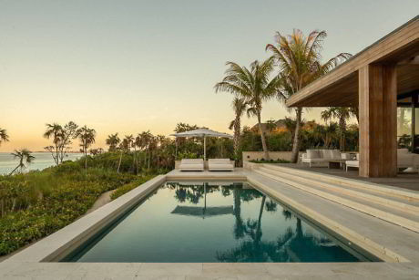 Modern poolside with loungers, wood-paneled patio, and ocean view at