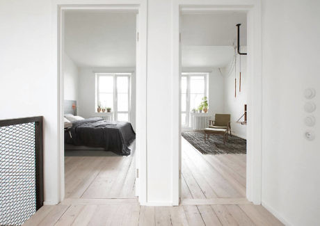 Minimalist white room seen through an open double doorway with light wooden floors.