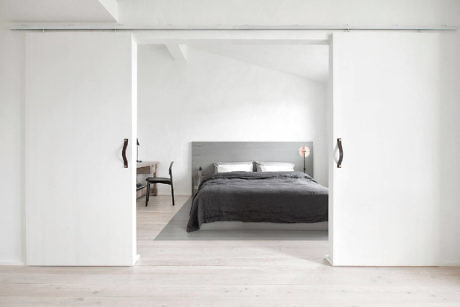 Minimalist bedroom with white sliding doors and pale wood floors.