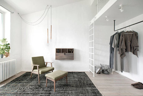 Minimalist white room with green chair, patterned rug, and wall-mounted clothing
