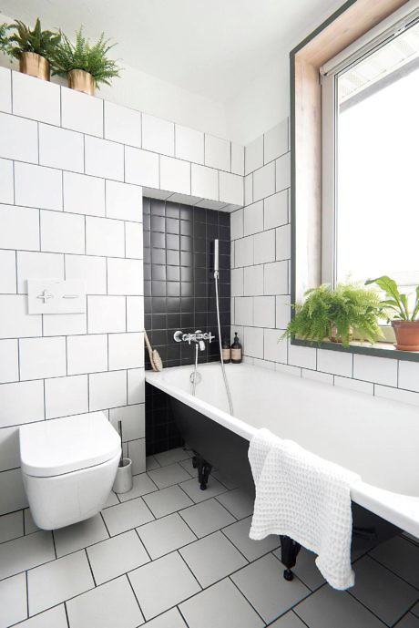 White tiled bathroom with a black and white claw-foot tub.