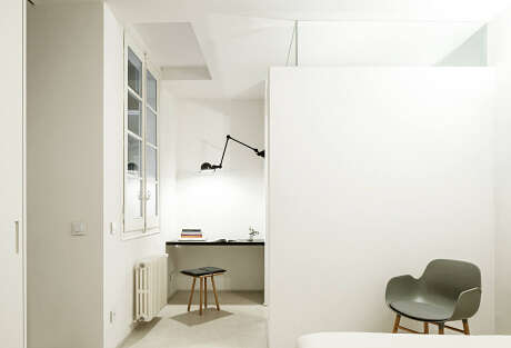 Minimalist workspace with glass windows, wooden stool, and a modern armchair against a neutral backdrop.