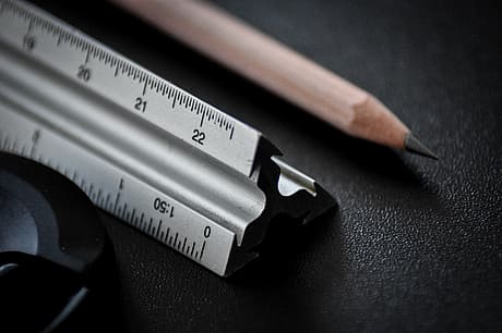 A close-up view of a metal ruler on a dark surface, with measurements and a pencil.