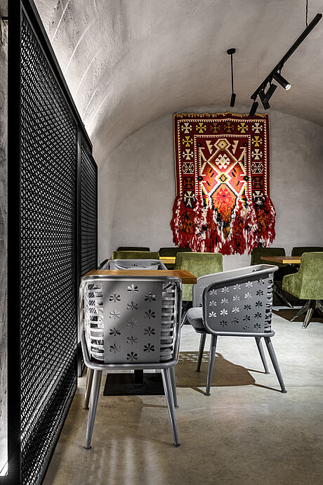 A cozy, textured lounge space with a decorative tapestry, seating, and lighting.
