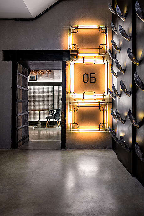 A dimly lit corridor with a decorative neon sign, textured walls, and a glimpse of a furnished room.