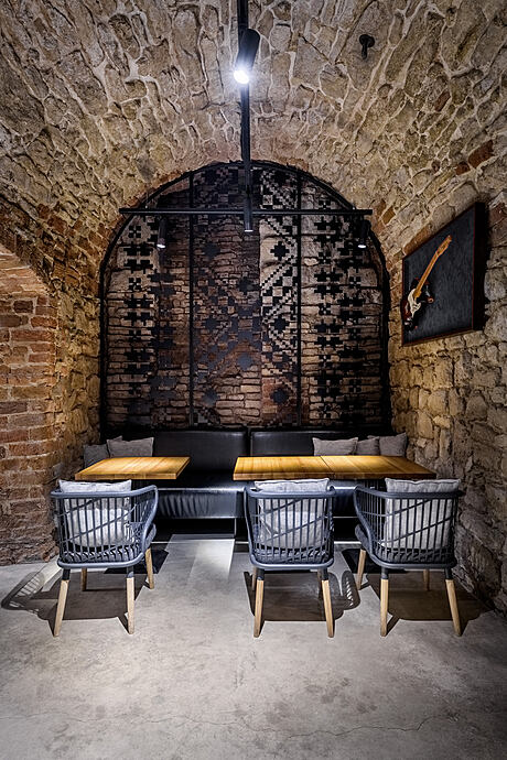 Rustic stone arched alcove with angular metal screen, wood benches, and leather chairs.