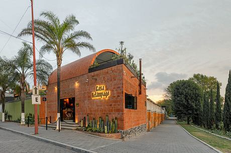 Modern brick building with arched roof and palm trees at twilight.