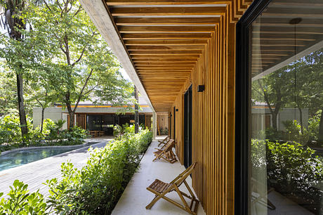 Modern home terrace with wooden beams, poolside view, and greenery.