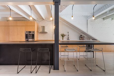 Modern kitchen with black counters, wooden cabinets, and industrial lighting.