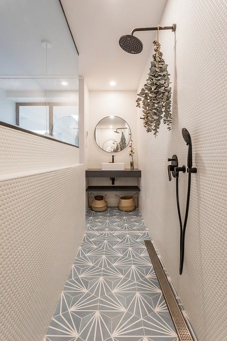 Modern narrow bathroom with patterned floor tiles and wall-mounted fixtures.