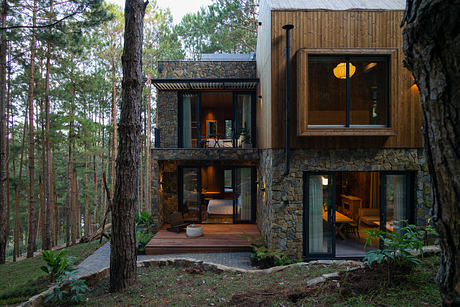 Modern two-story house with wooden and stone elements surrounded by trees.