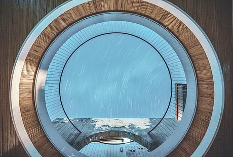 Circular skylight in a modern wooden interior design under a snowy sky.