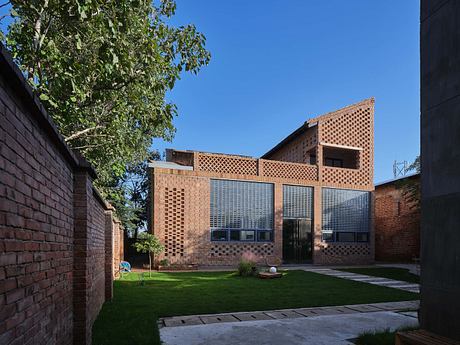 Modern brick building with patterned facade and large windows, amidst greenery.