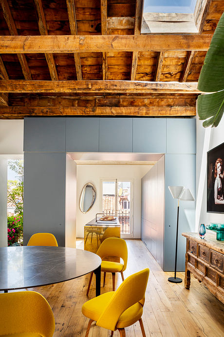 Modern dining room with yellow chairs, wooden ceiling beams, and rustic sideboard.