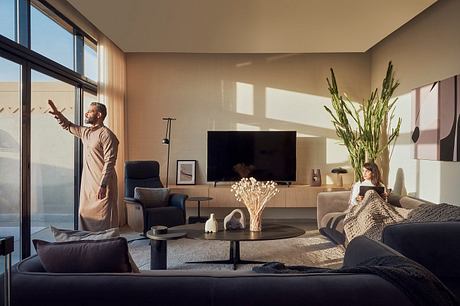 A man gestures by the window in a modern living room with a woman sitting on