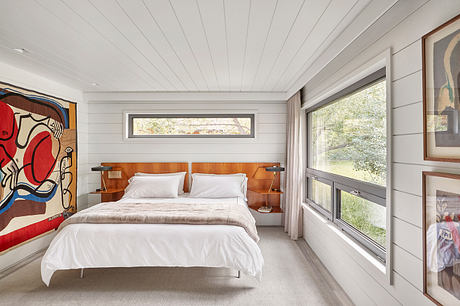 Modern bedroom with white bedding, wooden headboard, and colorful wall art.