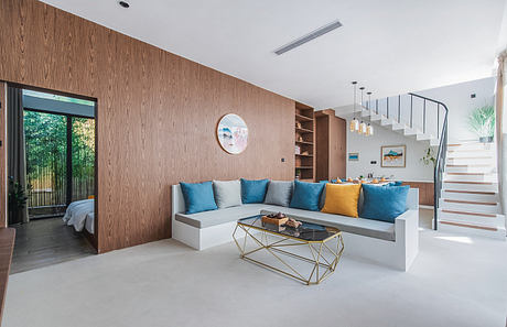 Modern living room with wooden wall paneling, colorful cushions, and minimalist stairs.