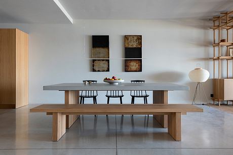 A minimalist dining room with a concrete table, wooden benches, and abstract wall art.