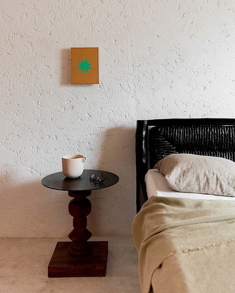 Simple bedroom corner with a round table, mug, and framed art on wall.