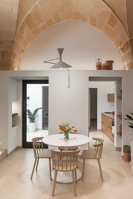 Minimalist dining area with arched ceiling, white walls, and wooden furnishings.
