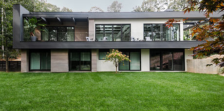 A modern, minimalist home with a sleek glass facade, surrounded by a lush, green lawn.