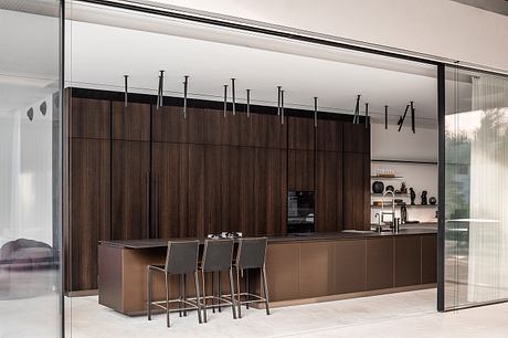 Sleek, modern kitchen design with dark wood panels, metal fixtures, and bar seating.