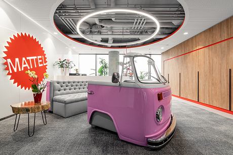 Vibrant, retro-inspired office space features a pink vintage van, neon signage, and modern furnishings.