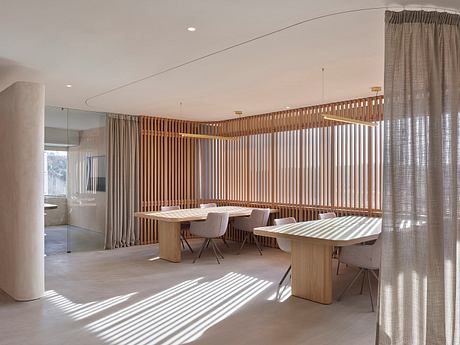 A modern, minimalist dining area with wooden slat partitions, natural lighting, and neutral furnishings.