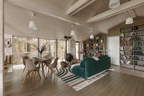 Cozy cabin interior with exposed wood beams, shelves, and large windows offering scenic views.