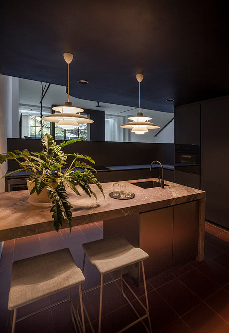 Well-lit, modern kitchen with sleek black cabinetry, pendant lights, and natural stone countertop.