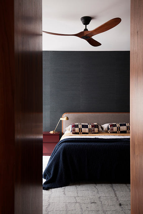 A cozy bedroom with a wooden ceiling fan, dark wall color, and patterned bed linens.