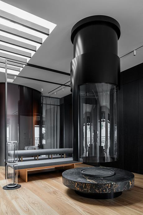 Sleek, minimalist interior with a striking, cylindrical glass-enclosed fireplace feature.
