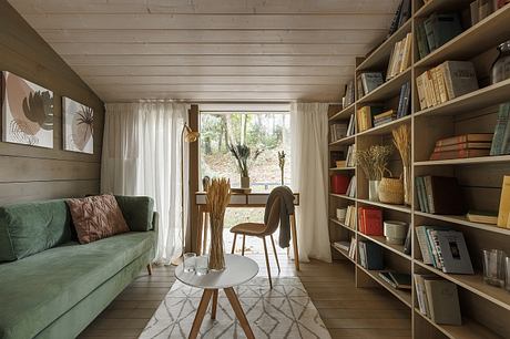 Cozy cabin interior with wooden beams, bookshelves, and a view of the forest outside.