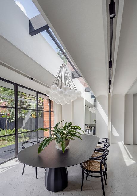 Sleek modern dining room with dramatic ceiling lighting, floor-to-ceiling windows, and lush greenery.