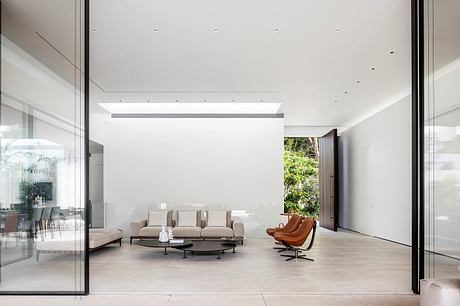 Bright, modern living room with large windows, minimalist furniture, and lush greenery outside.