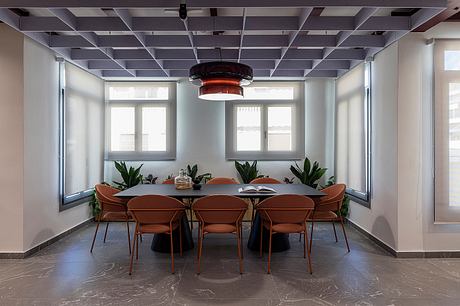 A modern office space with a sleek, minimalist design featuring floor-to-ceiling windows, exposed ceiling beams, and a stylish dining area.
