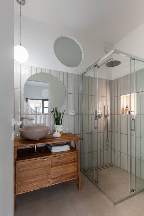 Sleek, minimalist bathroom with wood vanity, round mirrors, and glass shower stall.